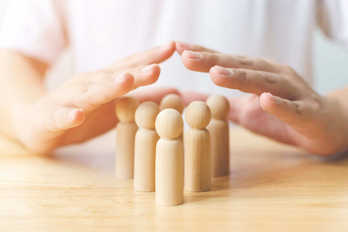 Two hands over group of wooden people on table-Dementia care team